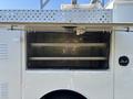 An open storage compartment of a white 2011 Ford F-550 with metal shelves inside