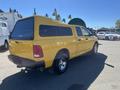 A yellow 2015 RAM 1500 pickup truck with a camper shell is parked with its rear facing the viewer and displays chrome wheels and a tailgate