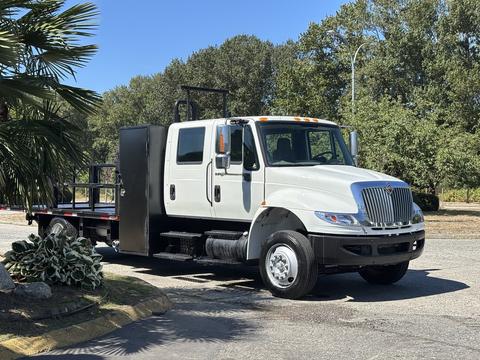 A white 2011 International 4300 flatbed truck with a cab and a large storage box on the side is parked at an angle