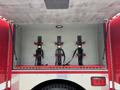A red emergency vehicle compartment with three black metal racks secured with yellow locking mechanisms and red straps on a diamond plate floor