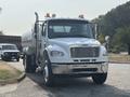 A white 2010 Freightliner M2 106 truck with a tanker attached is parked facing forward with lights on its roof