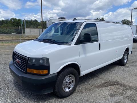 A 2023 GMC Savana van with a white exterior and black grille parked in a gravel lot