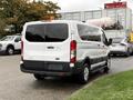 A 2018 Ford Transit van in white with a tall profile and rear windows, featuring alloy wheels and blue license plate holder