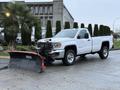 A 2017 GMC Sierra 3500HD pickup truck with a snow plow attached to the front parked on a wet surface