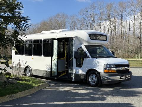 A white 2017 Chevrolet Express shuttle bus with an open door and large windows parked on the side of a road