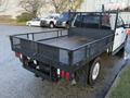 A 2020 Ford F-350 with a flatbed and metal mesh sides parked in a lot with a wooden floor in the bed and visible dual exhaust pipes