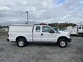 A 2015 Ford F-250 SD truck in white with a silver utility bed and a ladder rack on top parked on gravel