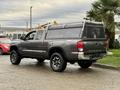 A gray 2016 Toyota Tacoma pickup truck with a camper shell and black alloy wheels parked at an angle with visible branding on the sides and rear