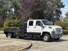 A white 2005 GMC C7500 Topkick truck with a flatbed and an orange light on the roof parked with a tool compartment on the side