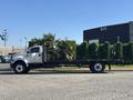 A white 2004 Ford F-750 flatbed truck with a palm tree loaded on the back parked on the street