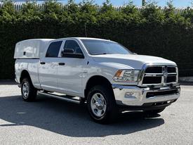 A white 2016 RAM 2500 pickup truck with a silver grill and canopy on the bed parked on a concrete surface