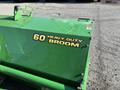 A green metal broom attachment labeled 60 HEAVY DUTY BROOM for a John Deere 1575 equipment