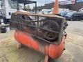 A rusty 2000 Baldor air compressor with a metal cage on top and an orange traffic cone resting on it