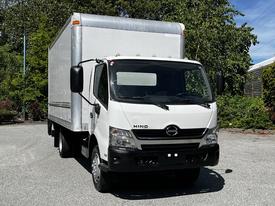 A 2018 Hino 195 box truck with a white cab and silver cargo area parked in a clear area