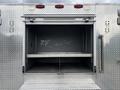 A 2010 Ford F-550 Super Duty with a silver metallic finish featuring a large storage compartment that is open and has two metal shelves inside