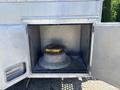 A large, circular metal object with a yellow and red top sits inside a storage compartment with an open door