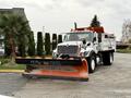 A 2012 International 7400 snow plow truck with an orange plow attached to the front and a dump bed in the rear