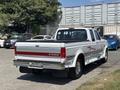 A white 1995 Ford F-250 pickup truck with a black bed cover and red stripe detailing parked with its back facing the viewer