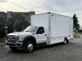 A white 2012 Ford F-550 truck with a large blank cargo box attached to the bed is positioned at an angle with its front facing the viewer