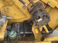 Close-up view of a hydraulic system featuring a black hydraulic pump and a green cap on a reservoir, with visible oil residue and metal components on a yellow machine
