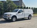 A white 2019 Ford F-150 pickup truck with a silver toolbox in the truck bed parked on a driveway