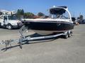 A 2013 Larson 238 boat on a trailer with a white and black hull and a covered cockpit area