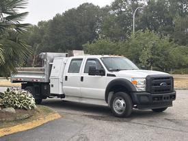 A white 2014 Ford F-550 truck with a flatbed and tool compartment on the side
