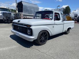 A vintage 1962 Ford 2WHDR pickup truck with a light gray body and black aftermarket wheels parked at a facility