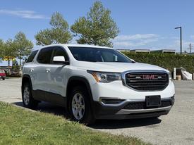 A white 2018 GMC Acadia parked on a road showcasing its distinctive front grille and sleek design with chrome accents and alloy wheels