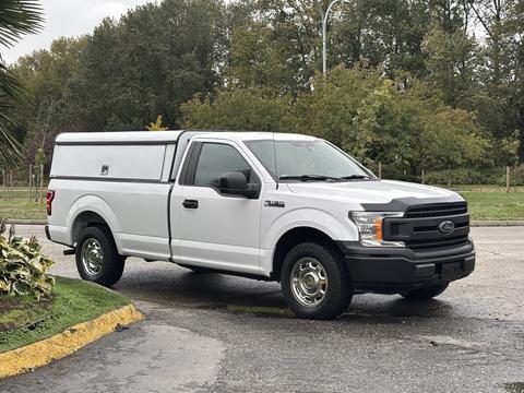 A white 2020 Ford F-150 with a camper shell on the bed parked with a slightly raised stance and silver wheels