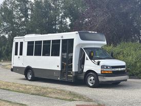 A 2020 Chevrolet Express bus with a white exterior and large windows parked with its door open