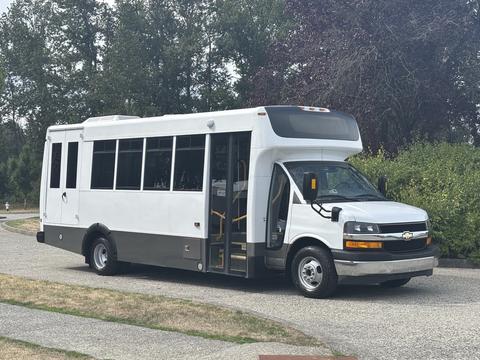 A 2020 Chevrolet Express bus with a white exterior and large windows parked with its door open