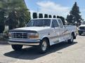 A 1995 Ford F-250 pickup truck in white with a silver stripe on the side and chrome accents parked on a road