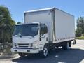 A white 2022 Isuzu NQR box truck with a large cargo area and a flat front design parked with its headlights and orange marker lights illuminated
