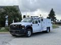 A white 2008 Ford F-450 utility truck with a service body and various tool compartments is parked with lights on its roof