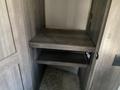 A wooden multi-tier shelf unit inside a recreational vehicle with two flat shelves and a side wall featuring an outlet and a door handle