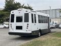 A white 2020 Chevrolet Express bus with large windows and a ramp on the side parked among other vehicles