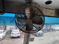 A black metal fan mounted on a pole inside a vehicle with visible blades and a circular grille