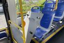 A 2017 Grande West Vicinity bus interior with blue seats and a folded gray table leaning against the yellow handrail
