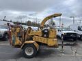 A yellow 2015 Vermeer Corporation BC1200XL wood chipper with a large chute and control panel is parked on a lot