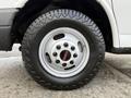 Close-up of a wheel from a 2015 GMC Savana featuring a silver rim with a red GMC logo and a rugged black tire with an aggressive tread pattern