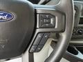 The steering wheel of a 2023 Ford E-450 with audio control buttons and a Ford logo displayed in the center
