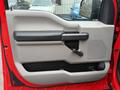 A red interior door panel of a 2015 Ford F-150 featuring a gray armrest a black handle and a manual window crank