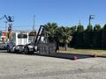 A white 2020 Peterbilt 330 truck with a flatbed and hydraulic arm extended for loading or unloading cargo