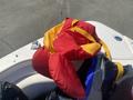 A red and yellow life jacket is draped over a boat seat with various colorful bags in the background