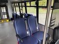 Interior view of a 2021 Ford Transit-350 featuring several rows of blue upholstered seats with seatbelts and a clear aisle in the center