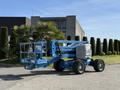 A blue 2012 Genie Z 45/25 telescopic boom lift with a basket raised is positioned on a paved area showcasing its four large wheels and articulated arm