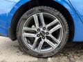 A close-up view of a silver alloy wheel on a blue 2021 Kia Forte featuring multi-spoke design and a black tire with brand lettering.