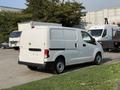 A white 2021 Nissan NV200 van is parked with its back facing the viewer showing sliding side doors and a simple design