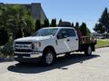 A 2019 Ford F-350 SD with a flatbed design parked with a spare tire in the bed and a red tool chest on the flatbed, featuring chrome accents and large wheels